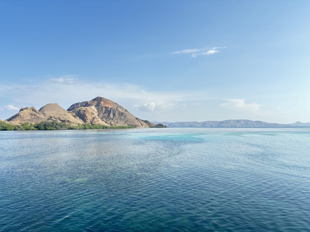 Scenic view of Komodo Islands with a hill and crystal blue ocean, taken from a liveaboard boat